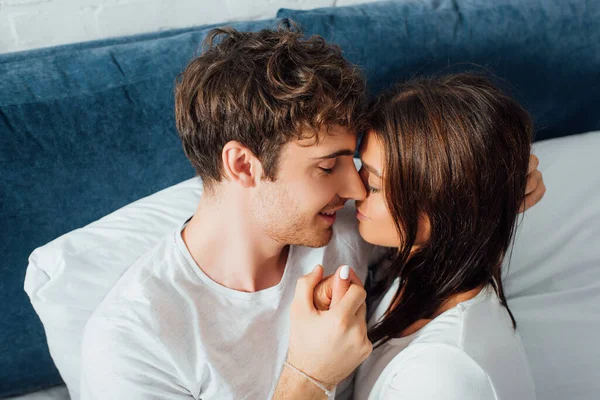 Vista de ángulo alto del joven con los ojos cerrados cogidos de la mano de su novia - foto de stock