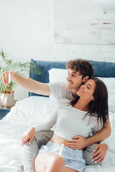 Joven abrazando novia y tomando selfie - foto de stock