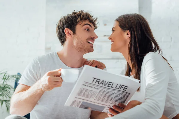 Enfoque selectivo del hombre sosteniendo una taza de café y periódico mientras mira a su novia en casa - foto de stock