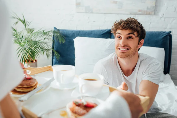 Избирательное внимание мужчины, глядящего на подругу с завтраком и кофе на трай в спальне — стоковое фото