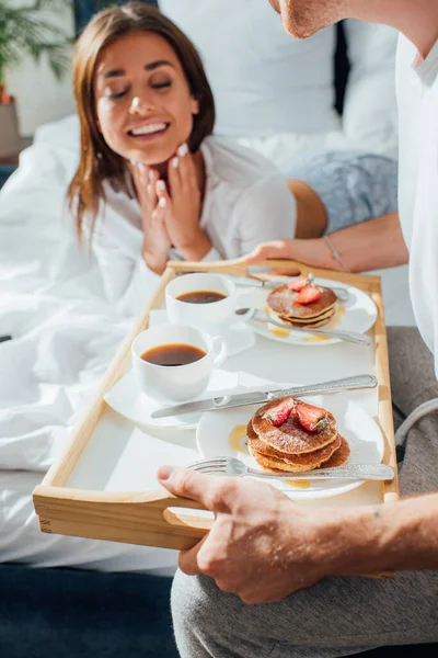 Selective focus of man holding breakfast on tray near woman on bed — Stock Photo