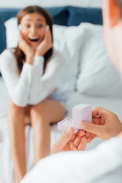 Selective focus of man holding engagement ring in box near woman on bed — Stock Photo