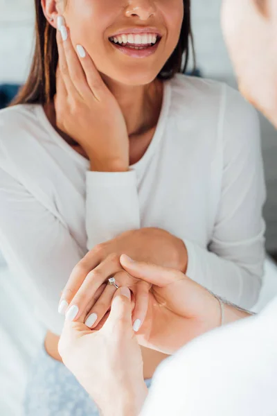 Cropped view of man wearing engagement ring on finger of girlfriend at home — Stock Photo