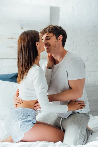 Mujer joven en pijama besando novio en la cama — Stock Photo
