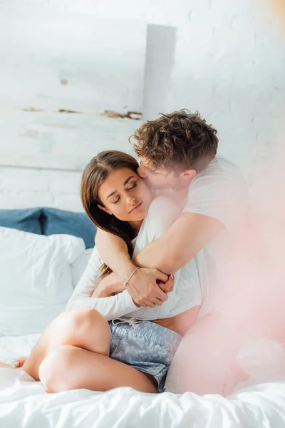 Foco seletivo de homem beijando na bochecha e abraçando namorada na cama — Fotografia de Stock