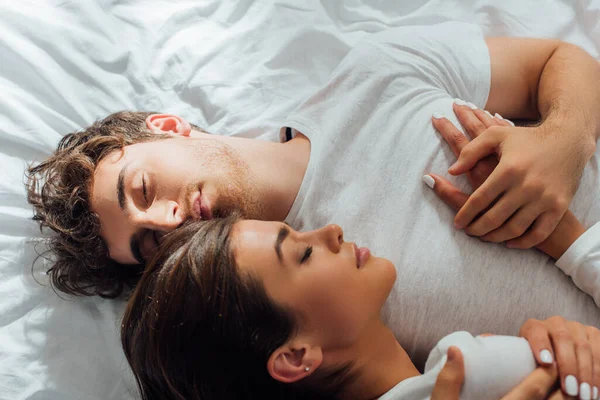 Vue du dessus du jeune couple embrassant les yeux fermés sur le lit — Photo de stock
