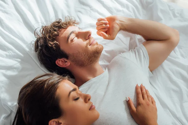 Draufsicht des Mannes dehnt sich, während er am Morgen neben schlafender Freundin auf dem Bett liegt — Stockfoto