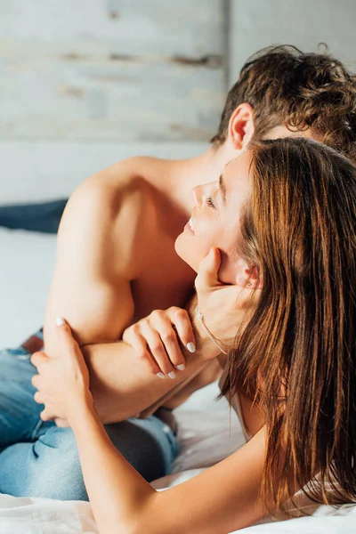 Selective focus of young shirtless man touching face of girlfriend on bed — Stock Photo