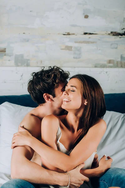 Shirtless homem de jeans abraçando jovem namorada com olhos fechados na cama — Fotografia de Stock
