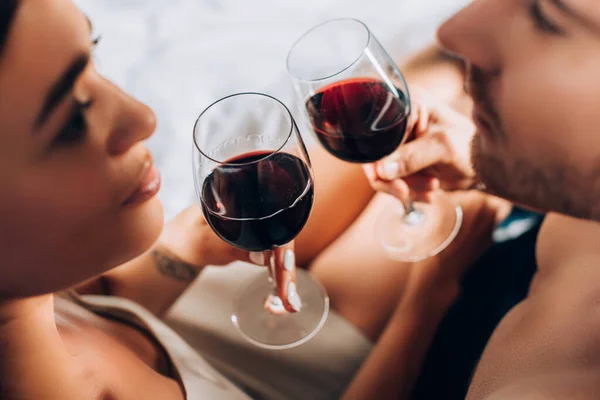 Selektiver Fokus des jungen Paares, das sich beim Anstoßen mit Wein im Bett anschaut — Stockfoto