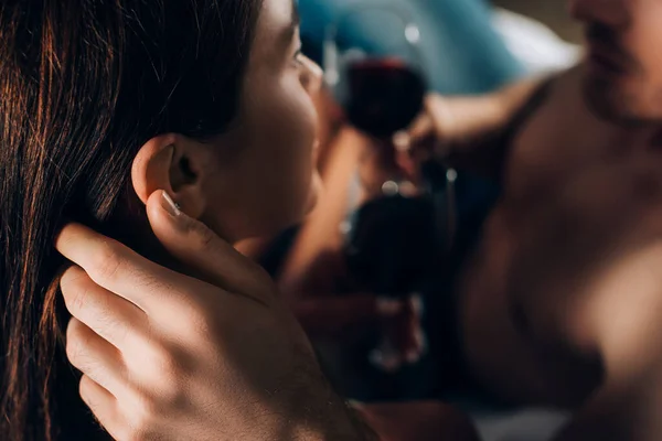 Fuoco selettivo di uomo senza camicia che tocca capelli di ragazza e tiene il bicchiere di vino — Foto stock