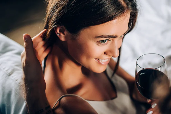 Selective focus of man touching hair of girlfriend with glass of wine on bed — Stock Photo