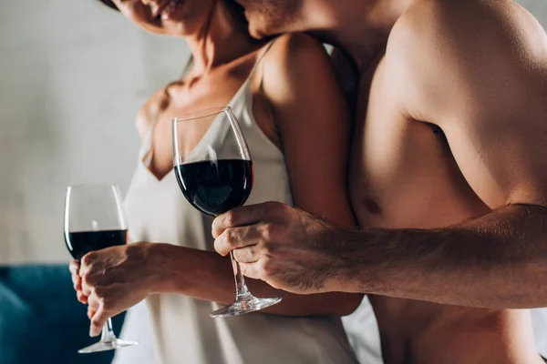 Vue recadrée d'un homme musclé tenant un verre de vin et embrassant une femme séduisante à la maison — Photo de stock