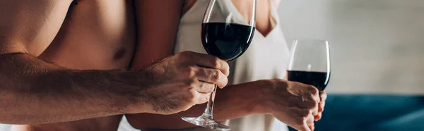 Panoramic crop of muscular man holding glass of wine near woman at home — Stock Photo