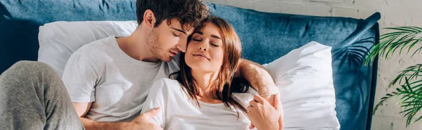 Panoramic concept of man hugging girlfriend in pajamas on bed — Stock Photo