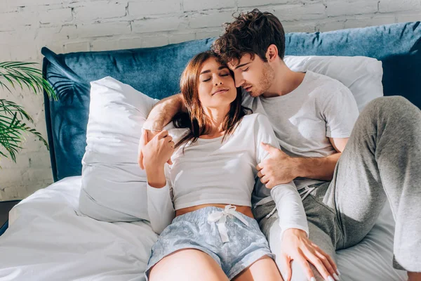 Young woman touching boyfriend in pajamas on bed at morning — Stock Photo