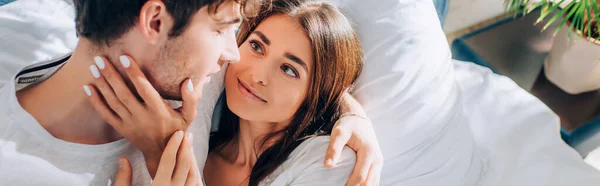 Vista panorámica de la joven mujer tocando el cuello del novio en la cama en casa - foto de stock