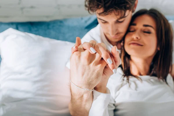 Выборочный фокус молодой пары, держащейся за руки на кровати — стоковое фото