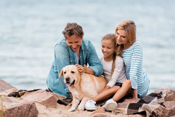 Selective focus of family with daughter petting golden retriever on seaside — Stock Photo