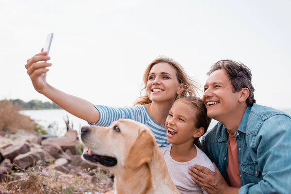 Foco seletivo da família com criança e golden retriever tomando selfie na praia — Fotografia de Stock