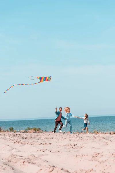 Enfoque selectivo de la familia con cometa corriendo en arena de playa durante las vacaciones - foto de stock