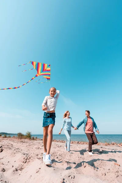 Selektiver Fokus von Mädchen mit Drachen in der Nähe von Eltern am Strand — Stockfoto