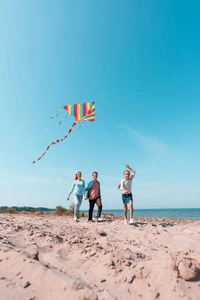 Selective focus of kid running with kite near parents on beach — Stock Photo