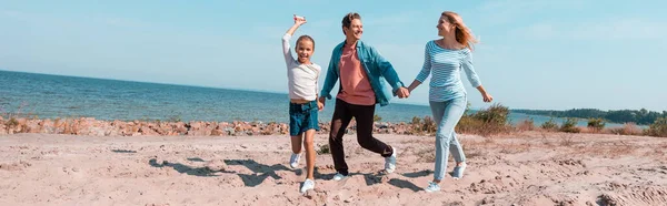 Cultura horizontal da família correndo na praia perto do mar durante as férias — Fotografia de Stock