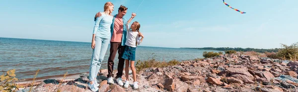 Horizontal image of man hugging wife and daughter on seaside during weekend — Stock Photo