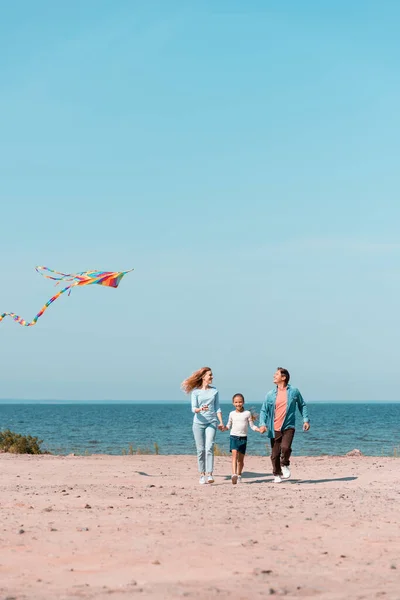 Focus selettivo della donna con aquilone che cammina vicino a figlia e marito sulla spiaggia — Foto stock