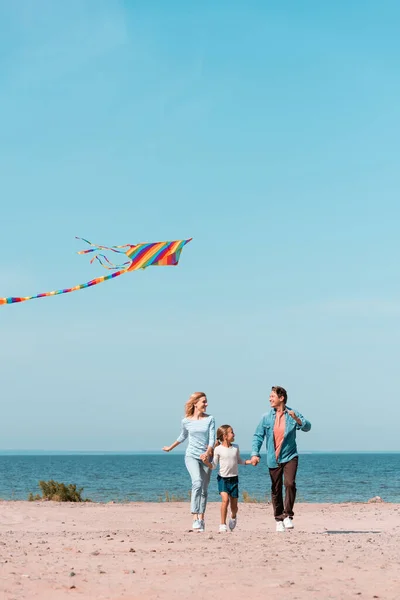 Selective focus of family running with kite on beach during vacation near sea — Stock Photo