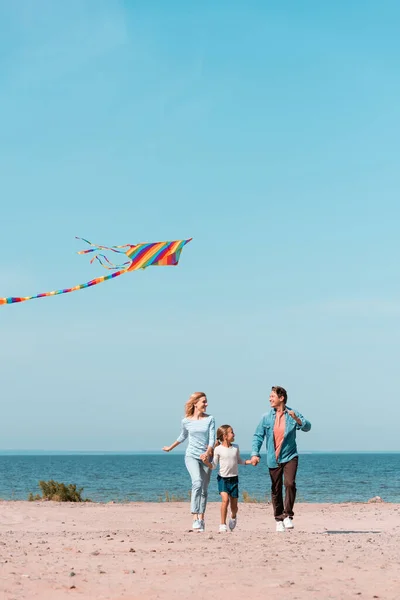 Focus selettivo della famiglia che corre con aquilone sulla spiaggia durante le vacanze vicino al mare — Foto stock