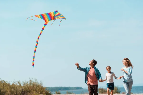 Девушка бежит рядом с родителями с воздушным змеем на пляже — стоковое фото