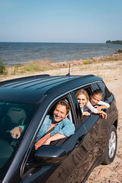 Hombre conduciendo coche cerca de la familia durante las vacaciones en la playa - foto de stock