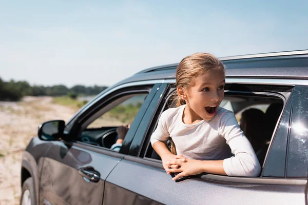 Выборочный фокус шокированного ребенка, смотрящего в сторону во время путешествия в машине с родителями — стоковое фото