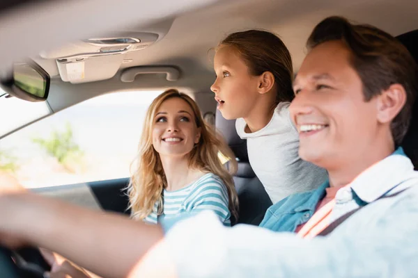 Selective focus of excited girl looking away while traveling with parents in car — Stock Photo