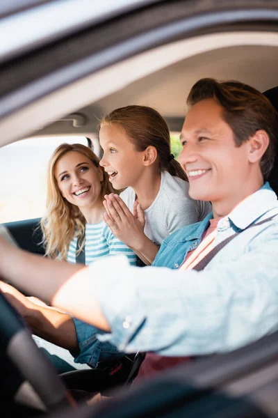 Selective focus of surprised kid looking away while sitting near parents in car during weekend — Stock Photo