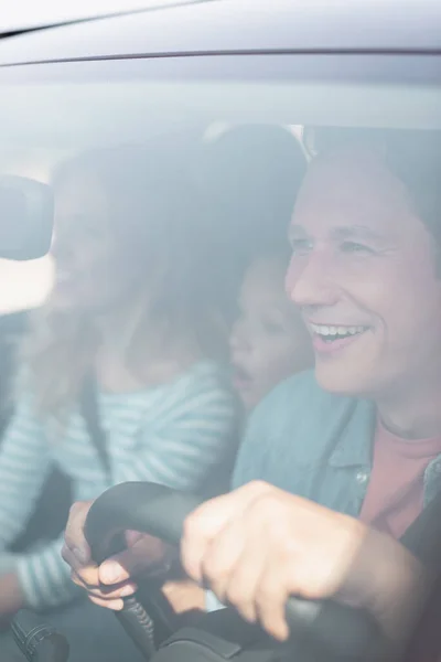 Selective focus of excited man driving car near family — Stock Photo