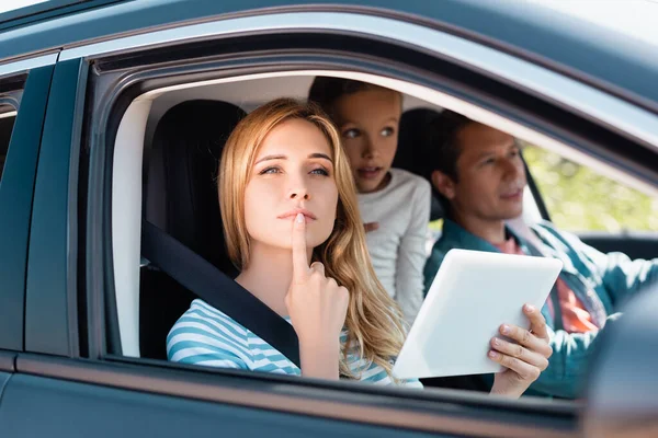 Selektiver Fokus der nachdenklichen Frau mit digitalem Tablet, die in der Nähe der Familie im Auto wegschaut — Stockfoto