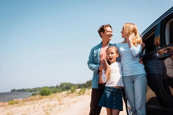 Selektiver Fokus von Mann umarmt Ehefrau nahe geschockter Tochter und Auto am Strand — Stockfoto