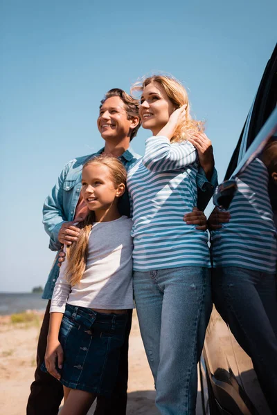 Enfoque selectivo del hombre abrazando esposa e hija cerca de coche en la playa - foto de stock