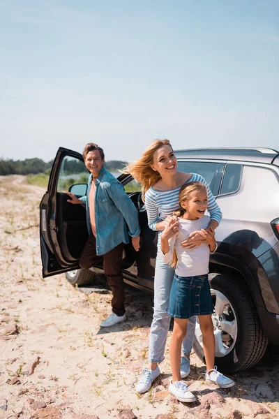 Focus selettivo di donna abbracciando figlia vicino marito e auto all'aperto — Foto stock