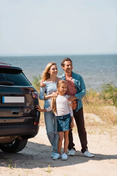 Concentration sélective des parents embrassant fille près de l'auto sur la plage près de la mer — Photo de stock