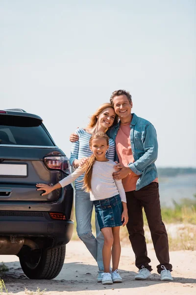 Concentration sélective de la famille regardant la caméra près de la voiture sur la plage — Photo de stock