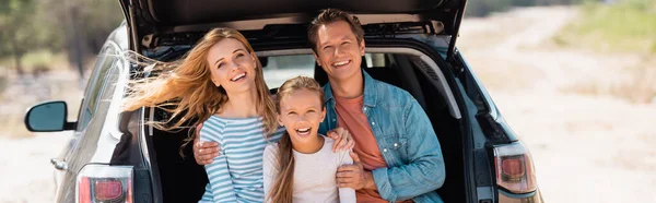 Панорамний знімок сім'ї, дивлячись на камеру, сидячи в багажнику на відкритому повітрі — стокове фото