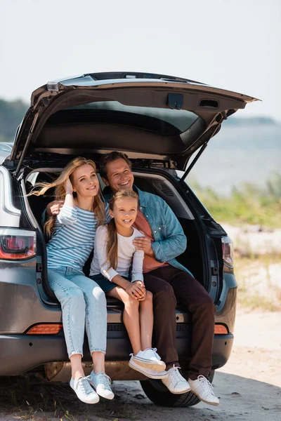 Family with daughter sitting in car trunk during vacation — Stock Photo