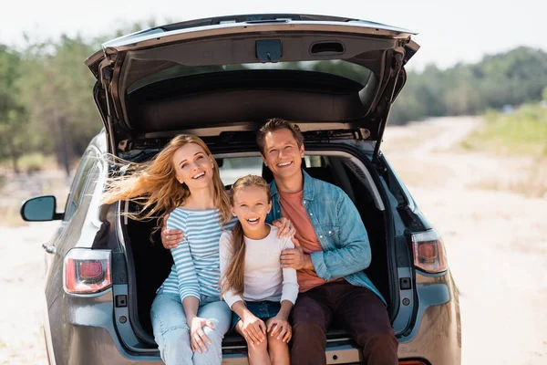 Parents embracing child while sitting in trunk of car during weekend — Stock Photo