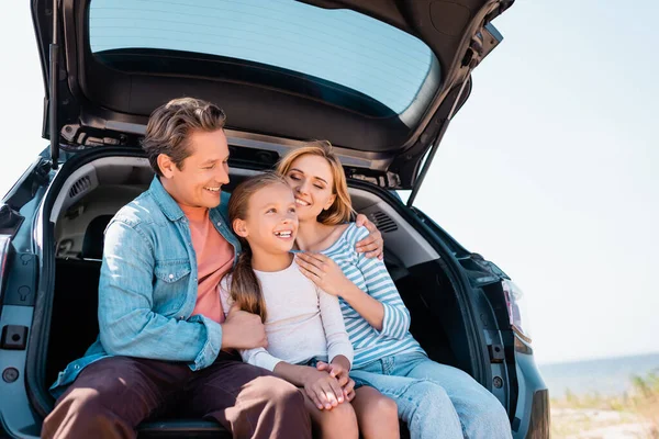 Man hugging wife and kid while sitting in trunk of car outside — Stock Photo