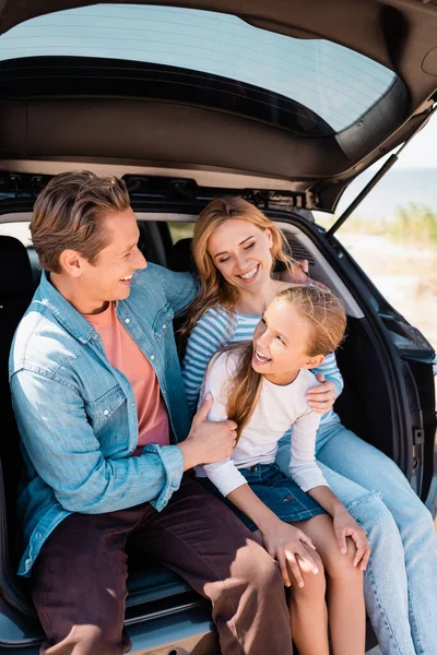 Выборочный фокус ребенка, сидящего рядом с матерью и отцом в багажнике автомобиля на открытом воздухе — стоковое фото