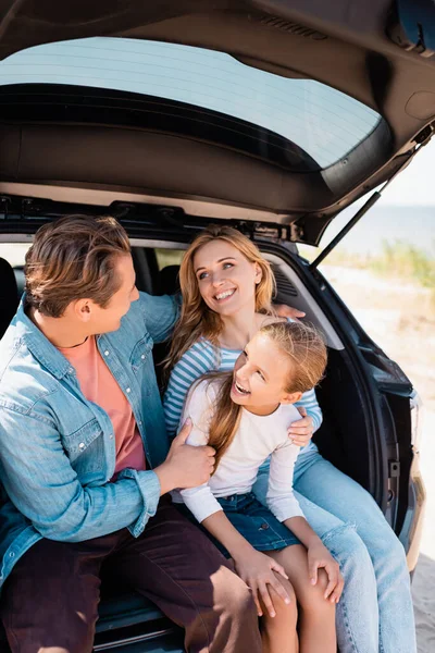 Girl sitting near parents in car trunk during weekend — Stock Photo